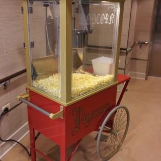 A vintage-style popcorn machine on a red cart with wheels, filled with fresh popcorn.