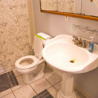 A small bathroom with a pedestal sink and toilet, featuring a tiled floor and a wall mirror.