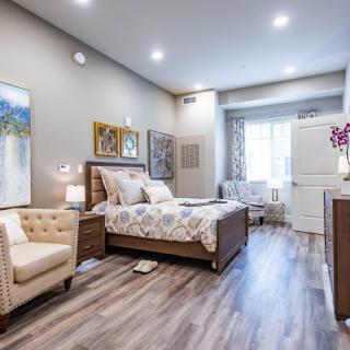 A modern and cozy bedroom featuring stylish furniture, artwork, and laminate flooring.