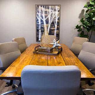 A modern conference room with a wooden meeting table, surrounded by chairs and decorated with wall art and indoor plants.