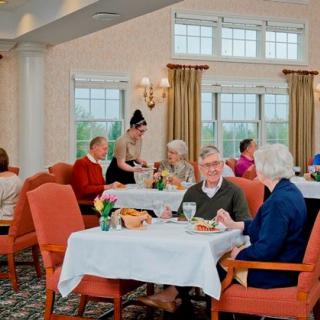 A group of seniors enjoying a meal in a restaurant setting with a waitress attending to their table.