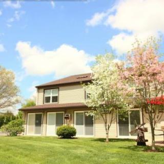 A suburban house with blooming trees and a well-kept lawn under a blue sky.