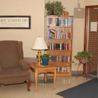 A cozy lounge area with a chair, bookshelf, and lamp.