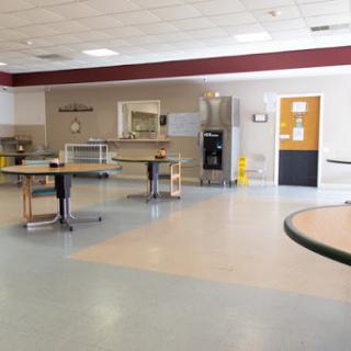A spacious and empty dining area with several tables, showing a clean kitchen in the background.
