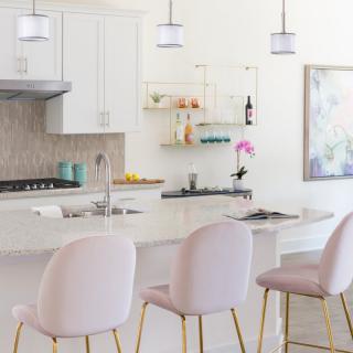 A modern kitchen featuring white cabinetry, pendant lighting, and a central island with pastel bar stools.