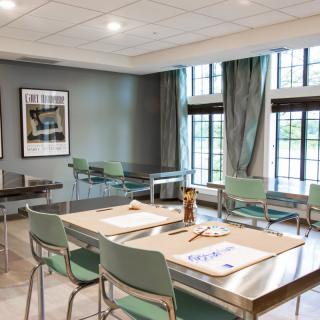 A well-lit art classroom with tables, chairs, and art supplies.