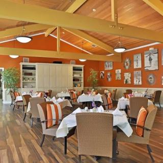 A cozy restaurant interior with neatly arranged tables and chairs, featuring warm orange walls and wooden flooring.