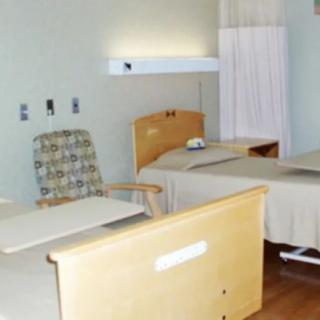 A clean and tidy hospital room with two beds and a chair.