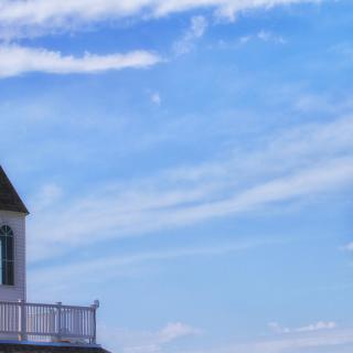 A lighthouse stands against a backdrop of blue sky and clouds.