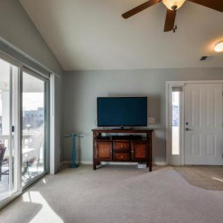 A spacious living room with a television, ceiling fan, and sliding glass door letting in natural light.