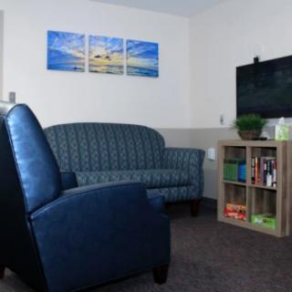 A cozy living room with a blue armchair, sofa, wall art, and a television beside a bookshelf.