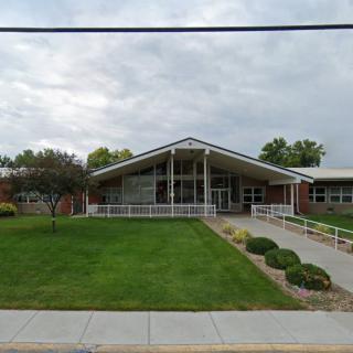 A building with a sloped roof and surrounding landscaped lawn under a cloudy sky.