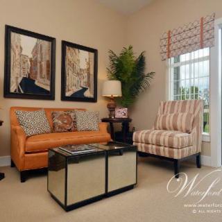 A cozy living room with a stylish orange sofa, striped armchair, and modern coffee table, complemented by artwork on the wall and natural light from the window.