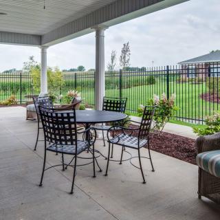 A spacious outdoor patio with metal table and chairs, overlooking a fenced garden.