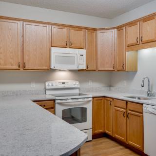 A kitchen with wooden cabinets, white appliances, and a light-colored countertop.