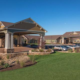 A large, modern building with a landscaped lawn and a parking lot under a clear blue sky.