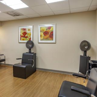 An interior view of a hair salon featuring chairs and hooded hair dryers with wall art and wooden flooring.