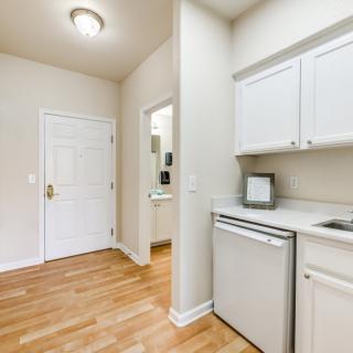 A compact kitchen area with white cabinets and hardwood flooring in an apartment.