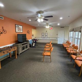 A spacious waiting room featuring orange chairs and walls, a television, and a foosball table.