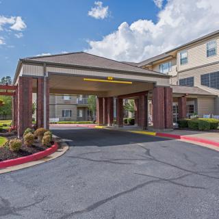 A view of a commercial building entrance with a wide driveway and well-maintained landscaping under a partly cloudy sky.