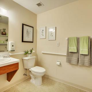 A clean and modern bathroom with a toilet, sink, and mirror. The walls are adorned with framed artwork and green towels hang neatly.