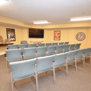 A small conference room with rows of chairs facing a television and framed pictures on the walls.