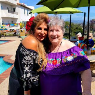 Two women in traditional clothing pose happily by a pool on a sunny day.