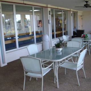 A covered patio area featuring a glass dining table with chairs and potted plants.