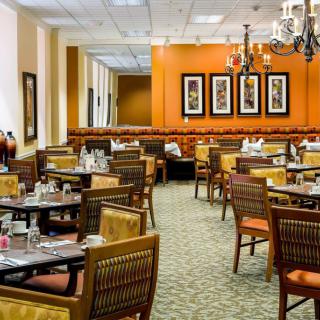 A well-decorated restaurant dining area with neatly arranged tables and chairs, featuring a warm color scheme and elegant lighting.