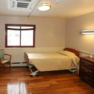 A clean and simple hospital room with a single bed, window, and wooden flooring.