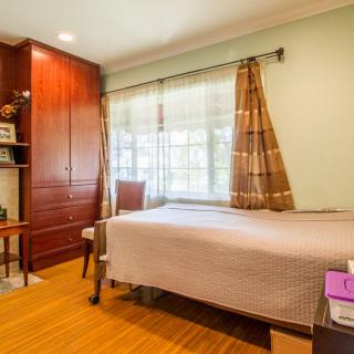 A cozy bedroom with a single bed, wooden wardrobe, and large window.