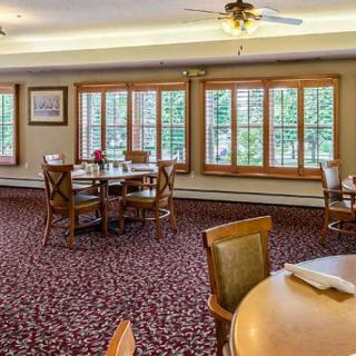 A spacious dining room with several tables and chairs, adorned with large windows and a decorative carpet.