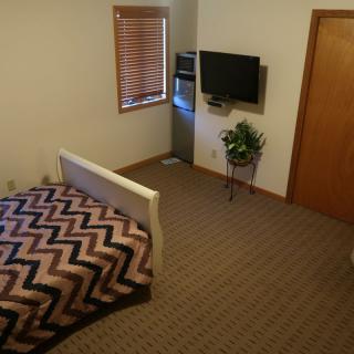 A cozy bedroom with a bed, television, and plant next to a window.