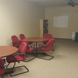 A meeting room with red chairs, round tables, and a projector screen.