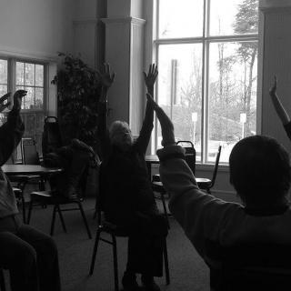 A group of seniors participating in a seated exercise session indoors.