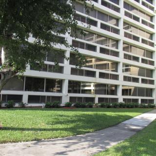 A high-rise building with large windows surrounded by a grassy area and sidewalk.