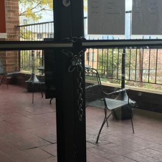 A locked door with a chain, revealing an outdoor area with empty chairs.