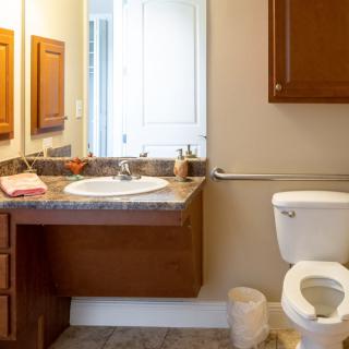 A clean and organized bathroom with a wall-mounted sink, countertop, toilet, and mirror.