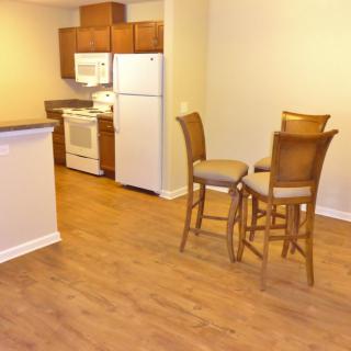 A cozy apartment kitchen and dining area with wooden flooring and simple furniture.