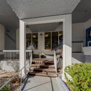 The image shows the entrance of a building with stairs leading up to it, surrounded by plants and a pathway.