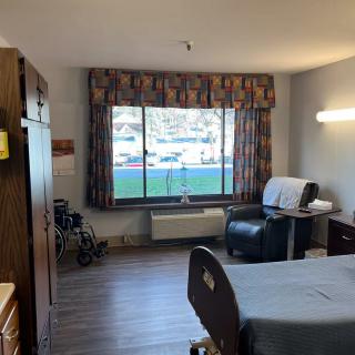 A hospital room with a bed, chair, window, and medical equipment.