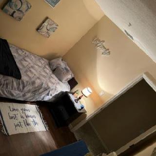 A cozy bedroom featuring a neatly made bed, wall art, and a bedside lamp.