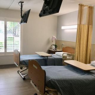 A hospital room with two beds, a privacy curtain, and TV screens.