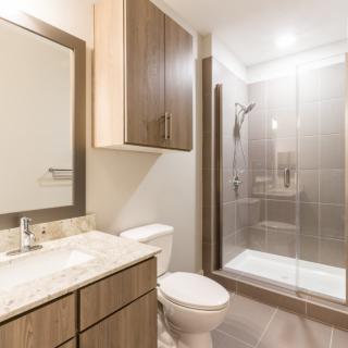 A modern bathroom with a glass-door shower, wooden cabinetry, and a marble-top vanity.