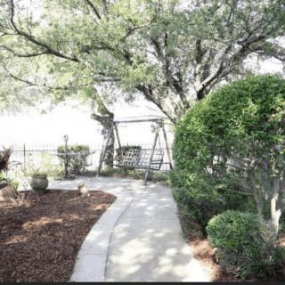 A serene garden pathway leading to a swing, surrounded by lush trees and manicured bushes.