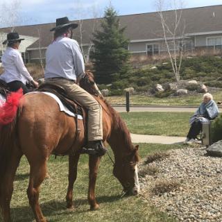 Two riders on horseback enjoy a sunny day in the park while another person watches.