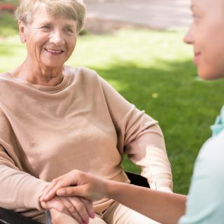 An elderly woman in a wheelchair smiling at her caregiver during an outdoor interaction.