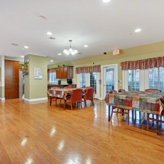 A spacious dining area with hardwood floors, featuring several tables and chairs, adjacent to a kitchen space.