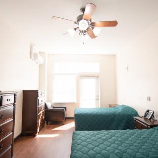 A bright bedroom with two beds, a ceiling fan, and ample natural light.