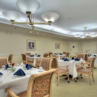 An elegant dining room with neatly arranged tables and chairs, featuring blue napkins and tasteful decor.